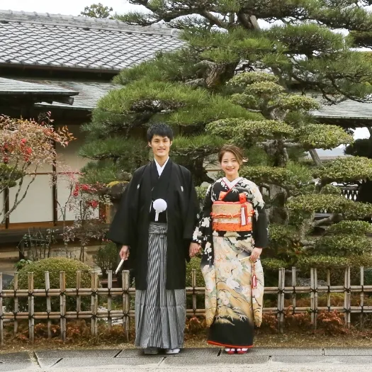 瓦屋根の日本家屋前に並ぶ和装のおふたり|伊勢おかげさま婚